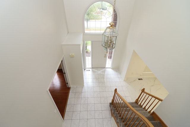 foyer entrance featuring light tile patterned flooring, a towering ceiling, baseboards, stairs, and an inviting chandelier