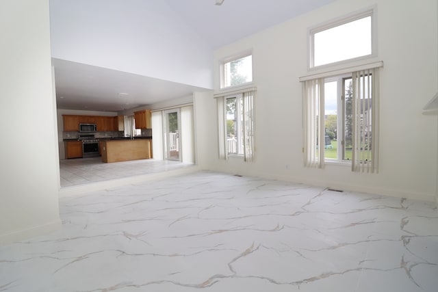 unfurnished living room with marble finish floor, high vaulted ceiling, and baseboards