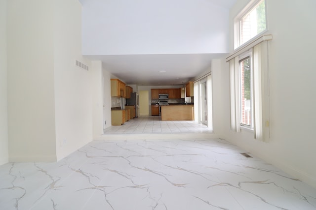 unfurnished living room with a towering ceiling, marble finish floor, baseboards, and visible vents