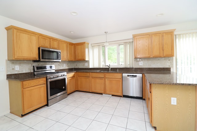 kitchen featuring a peninsula, a sink, appliances with stainless steel finishes, decorative backsplash, and pendant lighting