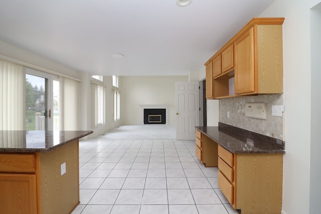 kitchen with a fireplace, light tile patterned floors, backsplash, open floor plan, and dark stone counters