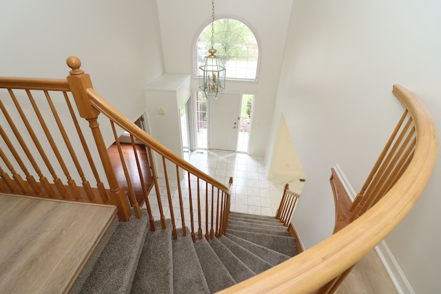 staircase featuring baseboards, a towering ceiling, and a notable chandelier