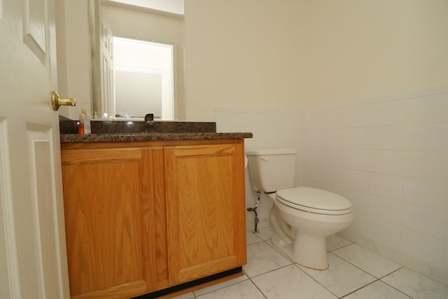 bathroom with tile walls, toilet, wainscoting, vanity, and tile patterned floors