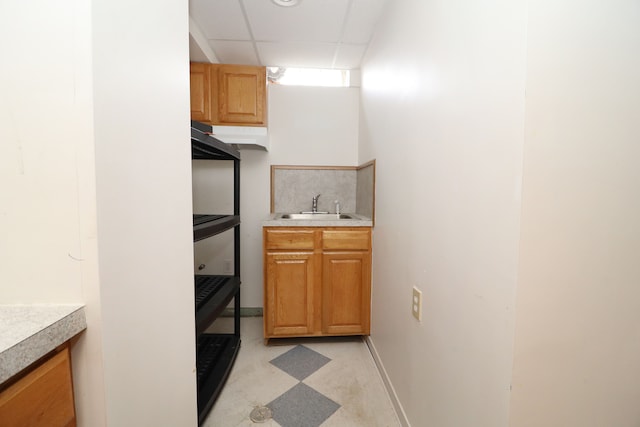 bar with light floors, a paneled ceiling, a sink, under cabinet range hood, and baseboards