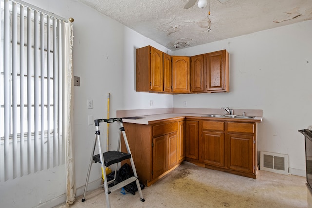 kitchen with visible vents, brown cabinetry, light countertops, a textured ceiling, and a sink