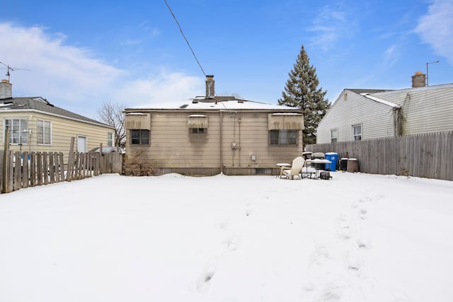 snow covered back of property featuring fence and a chimney