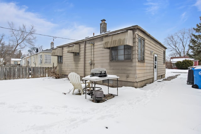 snow covered house with fence and a chimney