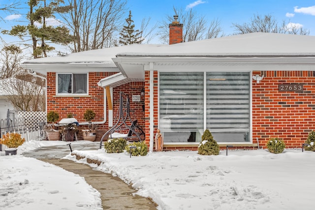 view of front of home featuring brick siding, a chimney, and fence