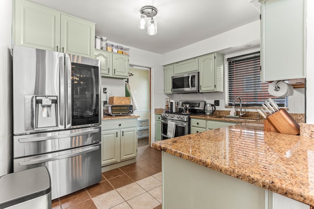 kitchen with light tile patterned floors, a sink, appliances with stainless steel finishes, light stone countertops, and green cabinetry