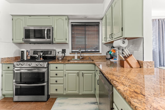 kitchen featuring green cabinetry, backsplash, light stone countertops, stainless steel appliances, and a sink