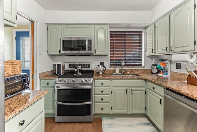 kitchen with light stone counters, stainless steel appliances, tasteful backsplash, a sink, and green cabinetry