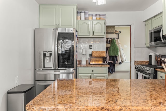 kitchen featuring green cabinets, stainless steel appliances, backsplash, and light stone countertops