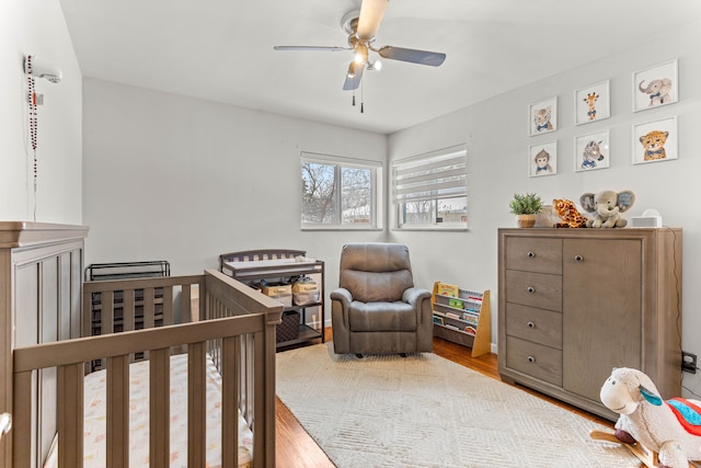 bedroom featuring light wood-style floors, a nursery area, and ceiling fan