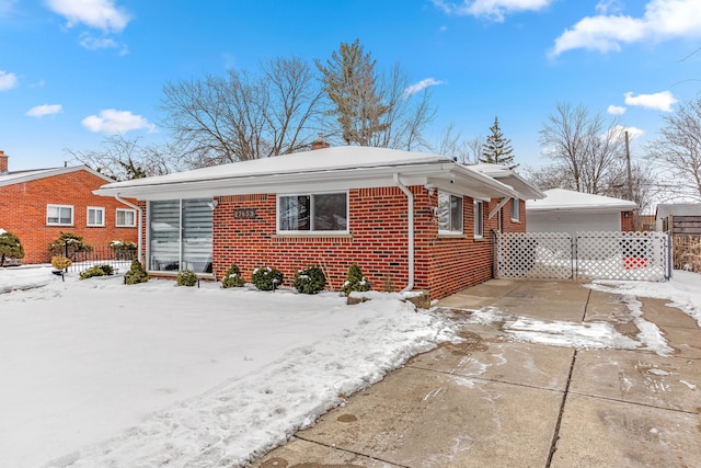 snow covered property with a garage, brick siding, fence, and a chimney