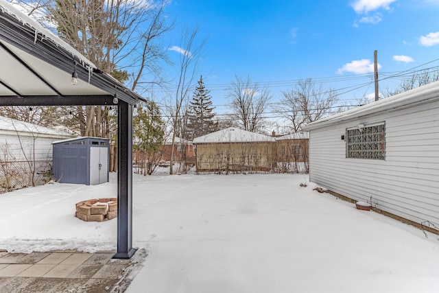 yard covered in snow featuring an outdoor structure, a fire pit, and a storage unit