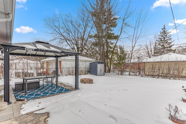 yard layered in snow with an outdoor fire pit, a storage shed, an outdoor structure, fence, and a gazebo