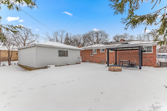 snow covered property with brick siding, an outdoor fire pit, a chimney, and a gazebo