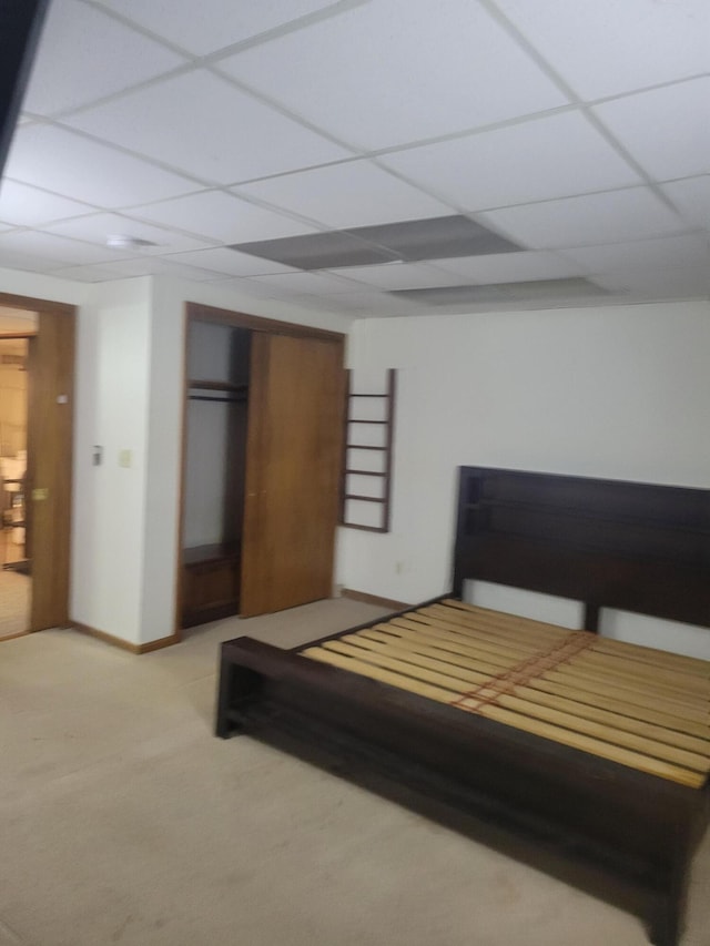 bedroom featuring baseboards, light colored carpet, a closet, and a paneled ceiling