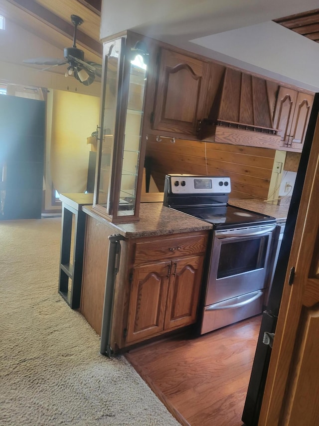 kitchen with brown cabinetry, light carpet, ceiling fan, stainless steel electric range, and premium range hood