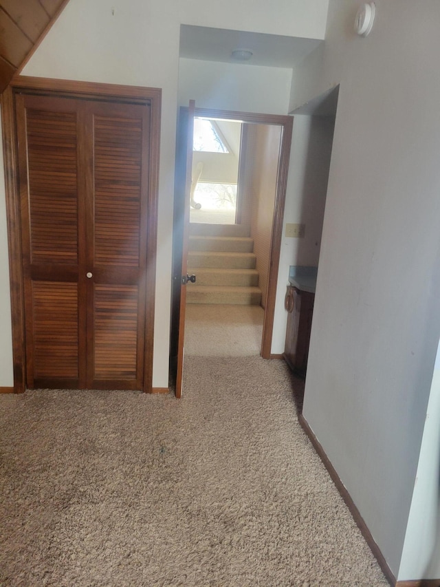 hall with baseboards, stairs, and light colored carpet