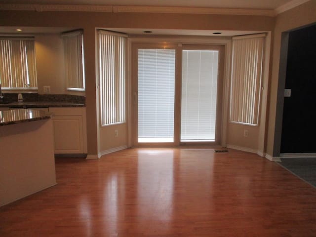 kitchen with baseboards, light wood-type flooring, dark countertops, and crown molding