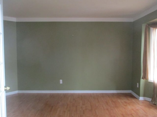 empty room with crown molding, light wood-style flooring, and baseboards