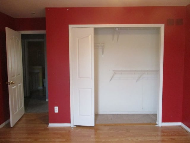 unfurnished bedroom with a closet, wood finished floors, visible vents, and baseboards