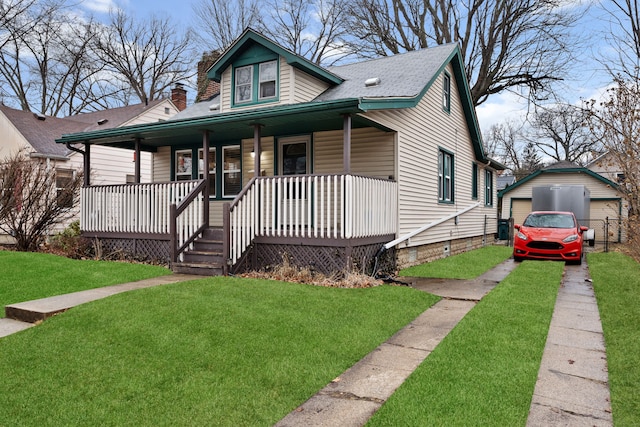 bungalow-style home with a detached garage, a porch, roof with shingles, an outbuilding, and a front lawn