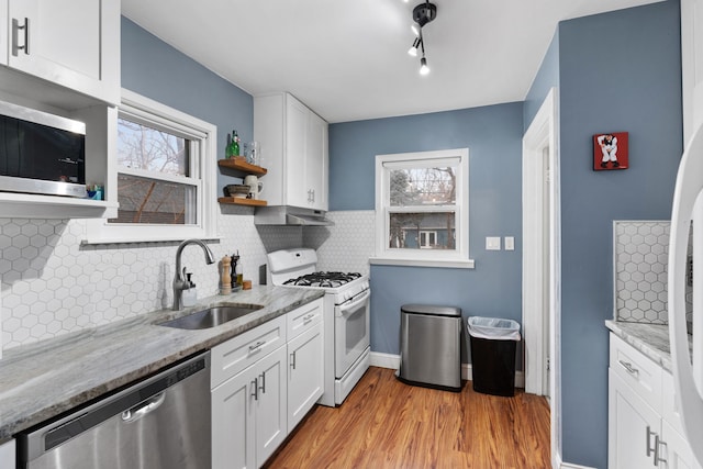 kitchen with appliances with stainless steel finishes, a sink, white cabinets, and light stone countertops