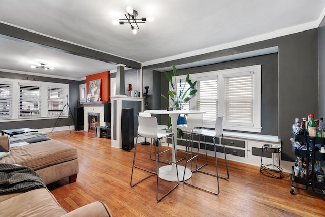 living area featuring a notable chandelier, a fireplace with flush hearth, ornamental molding, wood finished floors, and baseboards