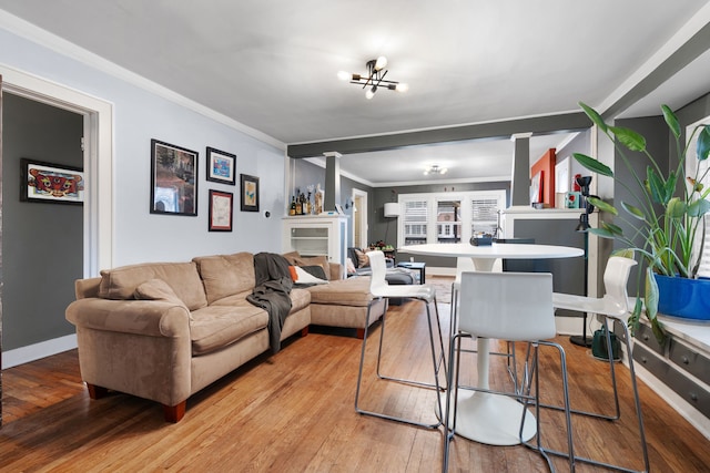 living area featuring light wood finished floors, baseboards, crown molding, and ornate columns