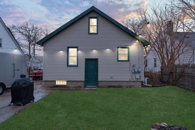 back of house at dusk with cooling unit, a yard, fence, and a patio