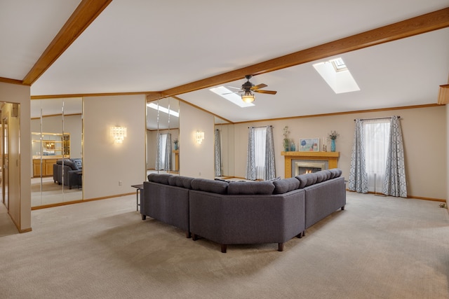 living area featuring ceiling fan, light colored carpet, baseboards, and vaulted ceiling with skylight