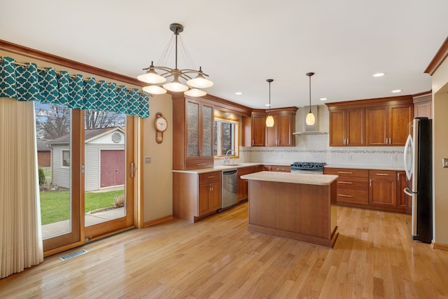 kitchen with visible vents, a center island, wall chimney exhaust hood, light countertops, and stainless steel appliances