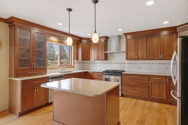 kitchen with wall chimney range hood, appliances with stainless steel finishes, brown cabinetry, and a sink