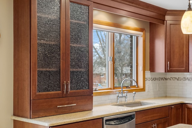 kitchen with backsplash, stainless steel dishwasher, brown cabinets, a sink, and glass insert cabinets