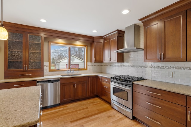 kitchen with decorative backsplash, wall chimney exhaust hood, a sink, light wood finished floors, and appliances with stainless steel finishes