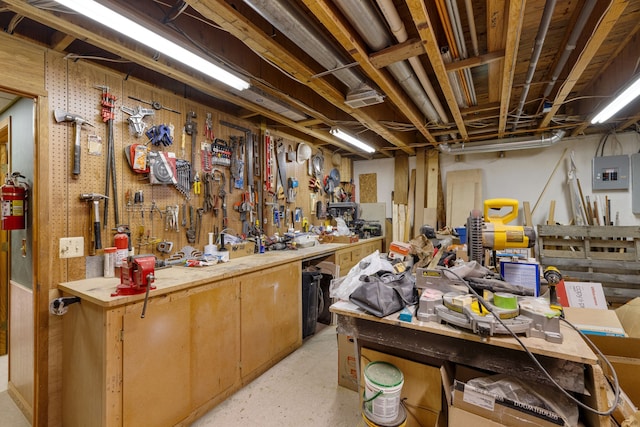 miscellaneous room with a workshop area, light floors, and electric panel