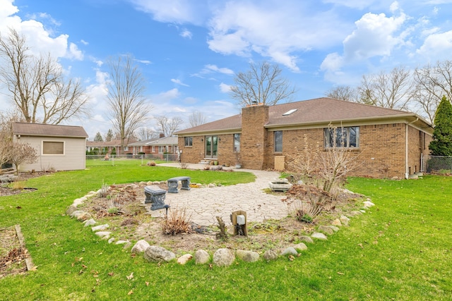 back of property featuring fence, brick siding, a chimney, a patio area, and a lawn