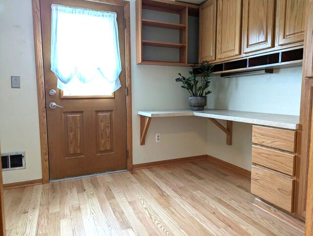 doorway to outside with visible vents, light wood-style floors, built in desk, and baseboards