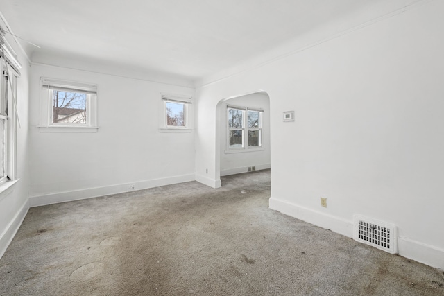 carpeted spare room with arched walkways, a wealth of natural light, visible vents, and baseboards