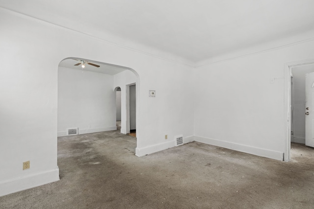 carpeted spare room featuring a ceiling fan, arched walkways, visible vents, and baseboards