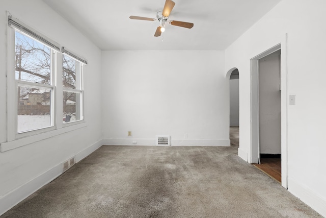 unfurnished room with baseboards, visible vents, arched walkways, ceiling fan, and carpet flooring