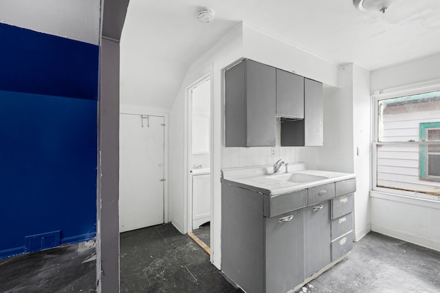 kitchen with gray cabinetry, a sink, visible vents, vaulted ceiling, and backsplash