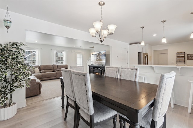 dining space with a lit fireplace, light wood finished floors, and an inviting chandelier