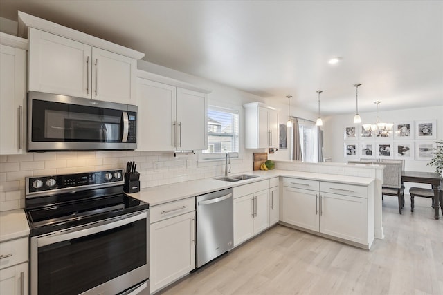 kitchen with white cabinets, a peninsula, stainless steel appliances, light countertops, and a sink