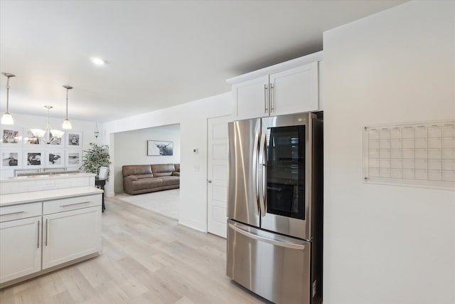 kitchen featuring decorative light fixtures, light wood finished floors, light countertops, refrigerator with glass door, and white cabinets