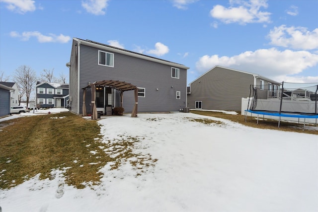 snow covered rear of property with a trampoline, a pergola, and a yard