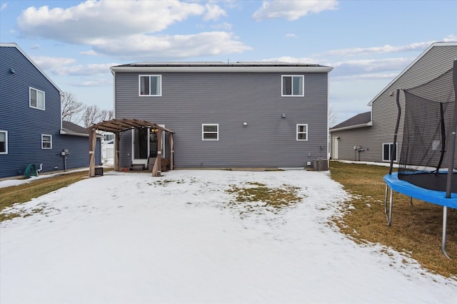 snow covered back of property with central air condition unit, a trampoline, and a pergola