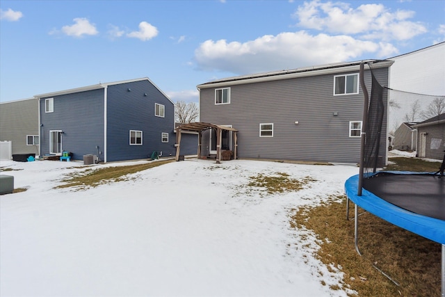 snow covered house featuring a trampoline, central air condition unit, a garage, and a pergola